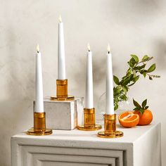 four candles are sitting on top of a white table with oranges next to it