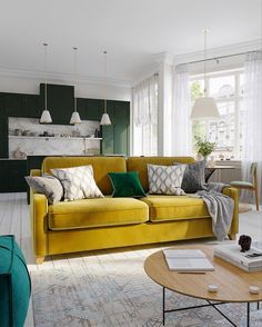 a living room with yellow couches and green chairs in front of a kitchen area