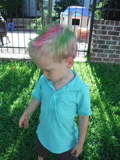 a little boy with pink and green hair standing in the grass