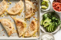 some food is laying out on a baking sheet with avocado, sour cream and salsa