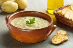 a brown bowl filled with soup next to some bread and other food on a table