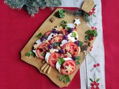 a wooden cutting board topped with sliced tomatoes and other vegetables on top of a red table cloth