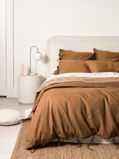 a bed with brown sheets and pillows in a white room next to a rug on the floor