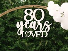 a sign that says 80 years loved with balloons in front of some bushes and trees