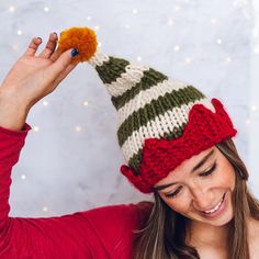 a woman wearing a knitted christmas hat with an orange pom - pom