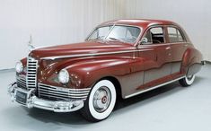 an old red car is parked in a room with white walls and carpeting on the floor