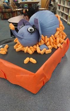 a table topped with an orange and blue cake covered in candy worms, eyes and ears