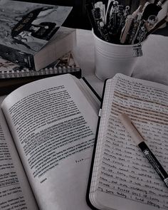 an open book sitting on top of a table next to a cup filled with pens