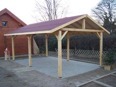 a wooden gazebo sitting in the middle of a yard next to a red building