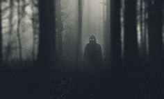 a person standing in the middle of a dark forest with fog and light coming from their eyes