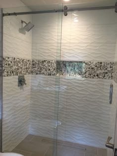 a glass shower door in a bathroom next to a white toilet and bathtub with tile on the walls