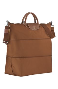 A zip inset expands and contracts a durable, water-resistant nylon travel bag trimmed with rich brown leather. Top zip closure. Removable crossbody strap. Interior wall pocket. Water-resistant lining. Folds flat for storage. Nylon with leather trim. By Longchamp; imported. Handbags.