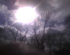 the sun shines brightly through the clouds above some bare trees on a cloudy day