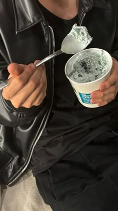 a man in black jacket eating ice cream from a bowl with a spoon on his lap