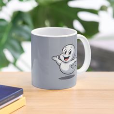 a coffee mug with a ghost on it sitting on a table next to a book