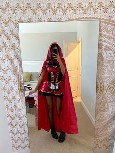 a woman dressed as a red riding hood and cape taking a selfie in front of a mirror