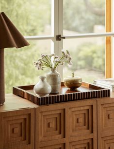 a table with vases and flowers on it in front of a window, next to a lamp