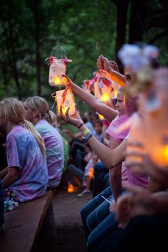 many people are sitting on benches and holding candles in their hands as they hold up mason jars