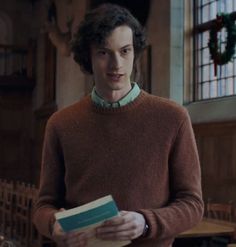 a man in a brown sweater holding a book