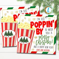 two red and white striped popcorn bags with christmas trees on them next to a pine tree