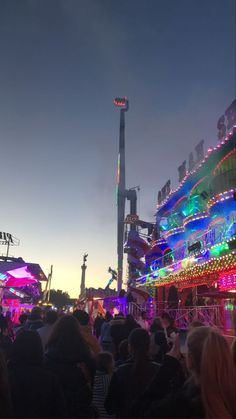 people are standing in front of an amusement park at night with lights on the rides