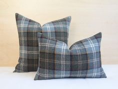 two gray plaid pillows sitting next to each other on a white tablecloth covered surface