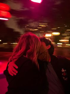 a man and woman are kissing in front of the camera at night with bright lights behind them