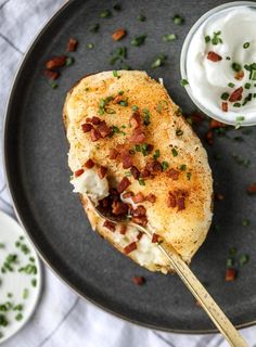 a black plate topped with food next to a small bowl of cream cheese and bacon