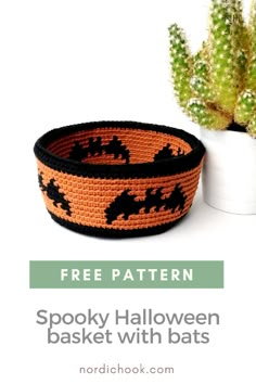 an orange and black woven bowl with bats on it next to a potted plant