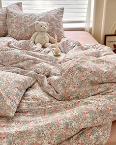 a teddy bear sitting on top of a bed next to pillows and blankets in a bedroom