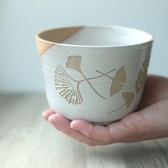 a hand holding a white bowl with gold designs on it