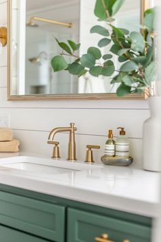 a bathroom sink with green cabinets and gold faucets on the counter top next to a mirror