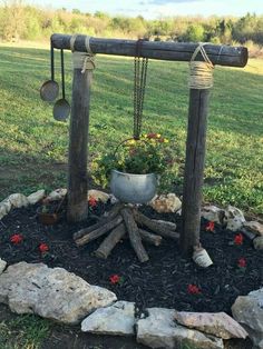 an outdoor fire pit in the middle of a field with rocks and flowers around it