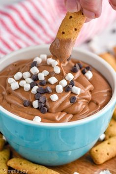 a hand dipping a cracker into a bowl of chocolate dip with marshmallows