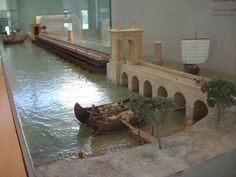 there is a model of a boat in the water next to a bridge and some trees