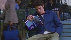 a man sitting on a park bench holding a book in his lap and looking at it