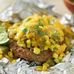 a piece of meat covered in corn on top of tin foil next to a bowl of lime wedges