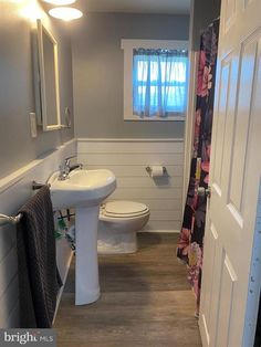 a bathroom with a toilet, sink and shower curtain in the doorway to another room