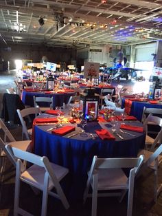 a room filled with tables and chairs covered in blue cloths, red napkins and place settings