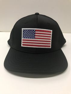 a black hat with an american flag patch on the front and back side, sitting on a white surface