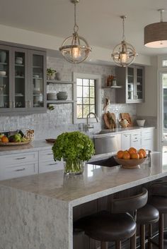 a kitchen with marble counter tops and stools in front of the island, surrounded by gray cabinets