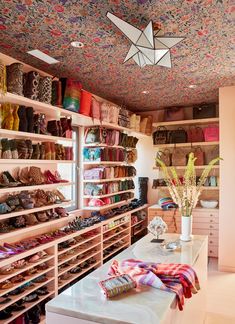 a room filled with lots of shoes and bags on shelves next to a vase full of flowers