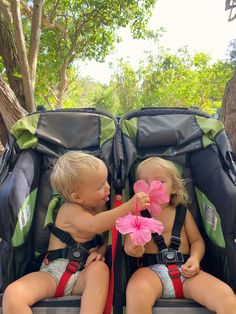 two toddlers sitting in the back of a stroller with pink flowers on it