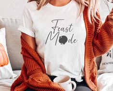 a woman sitting on a couch wearing a white t - shirt with the words feast mode printed on it