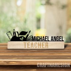 a wooden sign that says michael angell teacher on top of a table with a building in the background