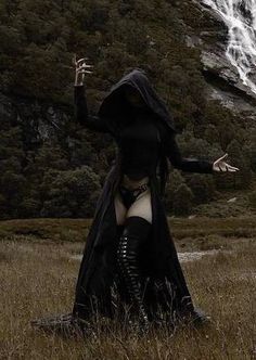 a woman dressed in black is standing in the grass with her arms outstretched and hands out