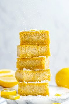 a stack of lemon bars sitting on top of a white table next to sliced lemons