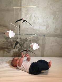 a baby laying on top of a bed next to a mobile that looks like birds