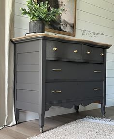 a black dresser with gold handles and drawers in a white living room, next to a painting on the wall