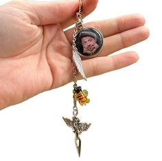 a hand holding a tiny necklace with a photo and angel charm on it's side